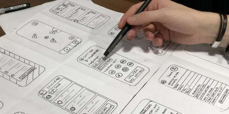 Hand holding a pen over mobile app sketches on paper